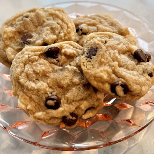 Four chocolate chip cookies on a pink glass dish